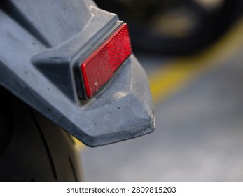 Close up detail of a red rectangular safety reflector mounted on the rear mudguard fender of a modern motorcycle or scooter parked outdoors