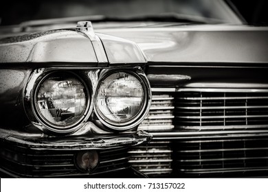 Close up detail of restored classic American car. Focus on headlights and hood. Retro vehicle in black and white.