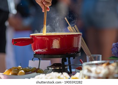 Close Up Detail Shot Of Person's Arm Stirring A Traditional Tasty Delicious Pot Of Hot Melted Liquid Swiss Cheese Fondue At An Outdoor Picnic In Switzerland Blurred Background Bright Colors Copy Space