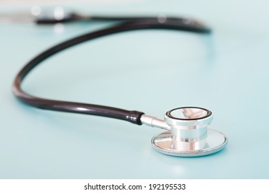 Close Up Detail Still Life View Of A Doctor Stethoscope Laying On A Plain Blue Background In A Hospital Table, Interior. Health And Medical Equipment And Insurance Icon With No People.