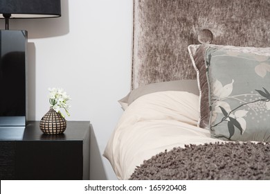 Close Up Detail View Of A Bed Head In An Elegant Hotel Bedroom With A Lamp And Side Table, Cushions And Pillows. Home Interior With No People.