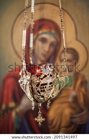 Close up detail view of christian hanging oil candle of brass and glass, hanging in church in front of religious iconography and iconostasis