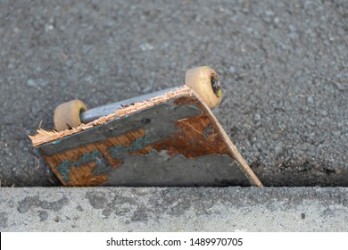 Close up detail view of the front section with the wheels on a broken skateboard deck pushed into a crack in the asphalt.