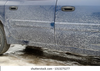 Close Up Detail Of Winter Salt Damage On The Side Of A Dark Blue Car Truck SUV Vehicle On An Icy Driveway Road.