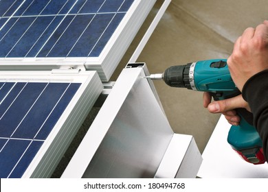 Close Up Detail Of Worker With Electrical Drill Or Borer Installing Windbreaker On Solar Panel Construction On A Flat Roof.