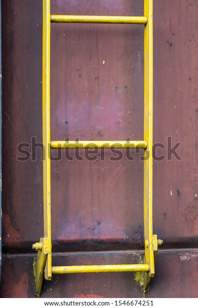 close up detail of a yellow steel or metal ladder
attached to the side of a rusty or rusted freight car on a train
showing a few rungs