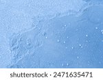 Close up detailed photo of snow and frozen water droplets siting ontop of a sheet of frozen blue ice.