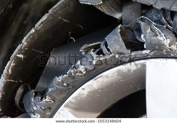 Close up details of a blown out tire with\
exploded, shredded and damaged rubber on a modern suv automobile.\
Flat low profile tyre on an alloy rim, ripped open in pieces with\
visible interior.