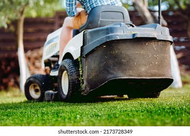 Close up details of landscaping and gardening. Worker riding industrial lawnmower
