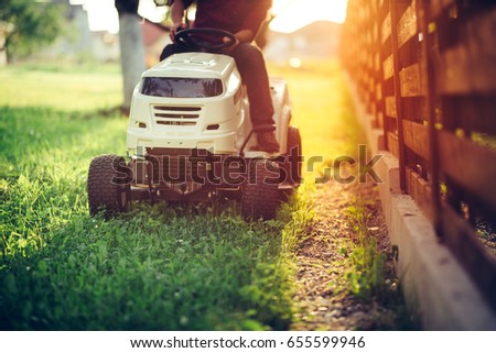 Close up details of landscaping and gardening. Worker riding industrial lawnmower 