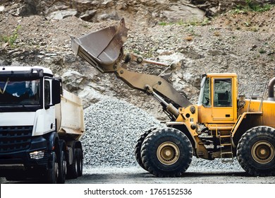 Close up details of wheel loader with scoop working on construction site and loading gravel on dumper trucks. Heavy duty bulldozer working