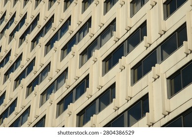 Close up diagonal view of a modern brutalist concrete skyscraper facade showing a geometric grid pattern of identical windows with dark glass.