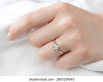 Close up Diamond ring on woman's finger before wedding with white scarf background.