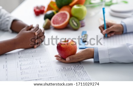 Close up of dietologist and patient female hands over doctor workplace, nutritionist holding apple