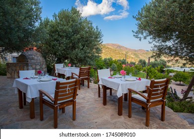 Close Up Dinner Tables On The Outside With A Great Mountain View With Blue Sky, Red Flower And Plates On Tables.