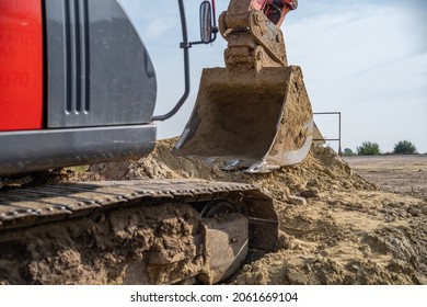 Close Up Dirt Excavator Bucket Digging Sandy Clay Soil During Construction. Red Crawler Against The Sky. Earthworks, Landscape Change, Paving The Road, And Communications