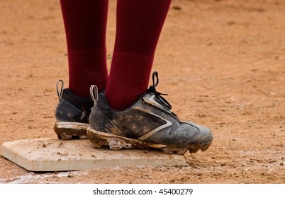 Close Up Of Dirty Baseball Cleats Standing On Base With Dark Red Socks