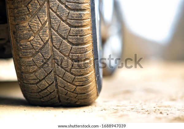 Close up of dirty car wheel with rubber tire covered\
with yellow mud.