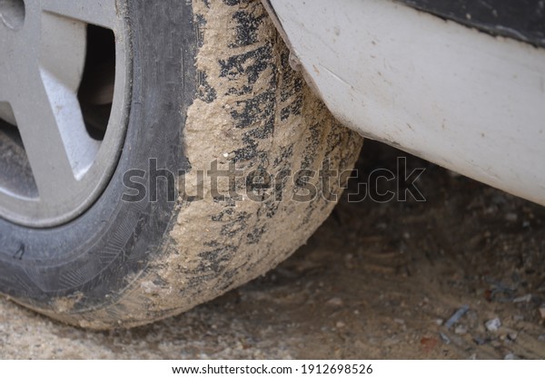 Close up of dirty car wheel with rubber tire covered\
with yellow mud.