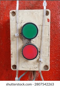 Close up of dirty industrial push button control panel with red and green buttons mounted on red wall. Old weathered switch box with cables and zip ties.