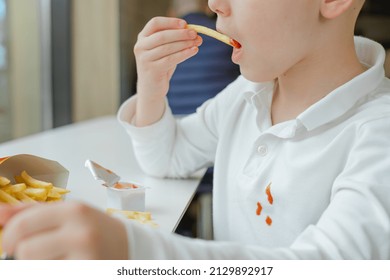 Close Up Of Dirty Ketchup Stains On White Kid Clothes. Boy Eating French Fries Potato Chips And Tomato Sauce At The Table In A Fast Food Restaurant. Kids Eat Unhealthy Fat Food. 