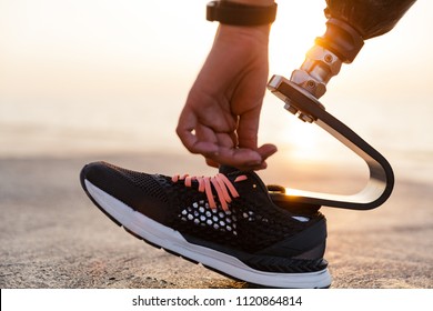 Close up of disabled athlete woman with prosthetic leg tying shoelace outdoor at the beach - Powered by Shutterstock