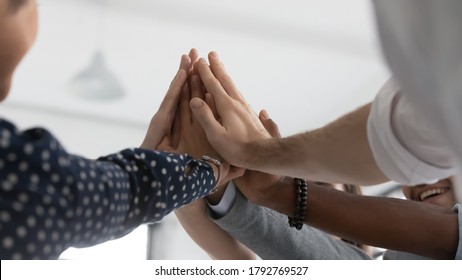 Close up diverse colleagues joining hands, giving high five at corporate meeting, celebrating sharing success, business achievement, goal, successful employees engaged in team building activity