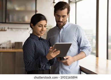 Close up diverse colleagues using tablet together, discussing online project, smiling Indian businesswoman and Caucasian businessman wearing glasses looking at device screen, standing in office - Powered by Shutterstock