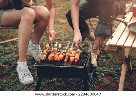 Close up diverse friends roasting bbq over charcoal stove at campgrounds, friends spending time together and enjoy camping on summer.