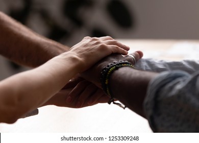 Close up diverse male female sitting holding hands together. Multiracial people starting common business or celebrate success at work stacked hands together showing unity support, all for one concept