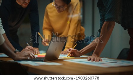 Close Up of Diverse Multiethnic Team Having Conversation in Meeting Room in a Creative Office. Colleagues Lean On a Conference Table, Look at Laptop Computer and Make Notes with Pencils on Notebooks.