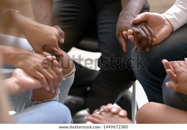 Close up diverse people sitting on chairs in\
circle, holding hands at group therapy counselling session,\
psychological help, trust and support, drug alcohol addiction\
treatment rehab concept