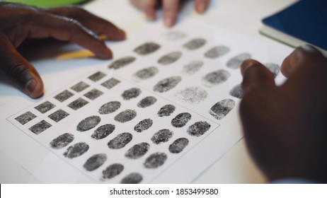 Close Up Of Diverse Police Officers Studying Fingerprint Card Working At Police Station. African And Caucasian Policemen Hands Pointing At Fingerprints Sample On Paper Investigating Crime In Office