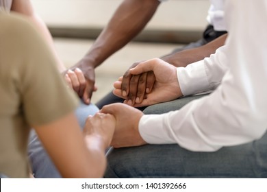 Close up of diverse religious people sit in circle hold hands pray together hope for help, multiracial men and women group gathering express support and understanding at psychological therapy session