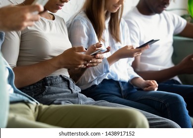 Close Up Of Diverse Young People Sit In In Queue Holding Cellphones Surfing Browsing Internet, Multiracial Millennial Friends In Row Using Smartphones Addicted To Social Media. Technology Concept