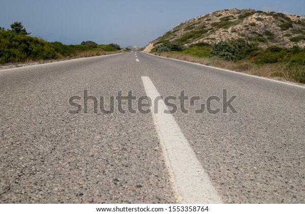 Close up of dividing line on asphalt road at\
summer.white lines on empty highway road with hills, mound. road\
surface.white line on asphalt road close up and clear blue sky.\
Travel concept. View from