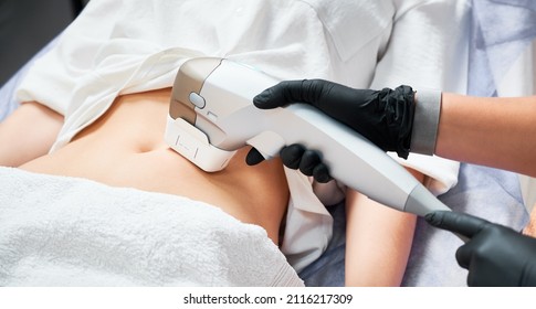 Close up doctor cosmetologist using ultrasound device while performing lifting procedure on woman abdomen. Female patient receiving body tightening and contouring procedure in cosmetology clinic.