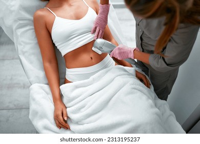 Close up doctor cosmetologist using ultrasound device while performing lifting procedure on woman abdomen. Female patient receiving body tightening and contouring procedure in cosmetology clinic. - Shutterstock ID 2313195237