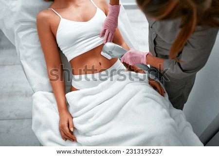 Close up doctor cosmetologist using ultrasound device while performing lifting procedure on woman abdomen. Female patient receiving body tightening and contouring procedure in cosmetology clinic.