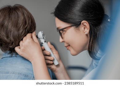 Close up of doctor examining boy's ear with otoscope in medical cabinet. Barotrauma laryngitis otitis ear treatment. Otorhinolaryngology concept - Powered by Shutterstock