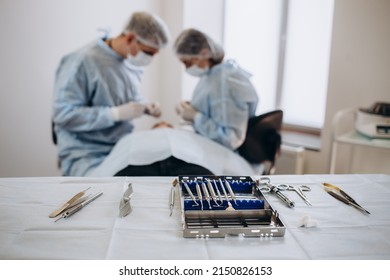 Close Up Of Doctor Hand Holding Forceps With Tampon While Surgeon And Assistant Performing Plastic Surgery On Blurred Background. Medical Team Using Various Surgical Instruments In Operating Room.