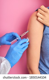 Close Up Of Doctor Hand Using Syringe To Make Vaccine Injection To Young Adult Female Patient, Isolated On Pink Background