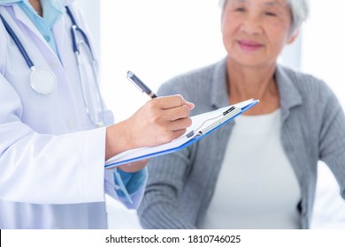 Close Up Of Doctor Hands With Clipboard Meeting In Medical Office And Senior Woman Background.