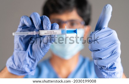 Close up of doctor hands with covid-19 booster shot syringe showing thumbs up - concept showing of recommendation of 3rd dose vaccination for immune weakened people.