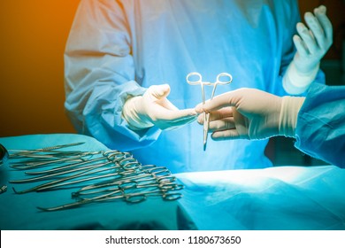 Close Up Of Doctor Hands During Surgery In Operation Room.Sterile Surgery Instruments Used In A Real Operation. Focus Is On The Row Of Clamp Handles.