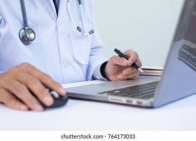 Close Up Of Doctor Holding Ballpoint Pen And Working On Laptop Computer On White Desk In Hospital, Electronic Health Records System EHRs, Electronic Medical Records System EMRs, Telemedicine Concept.