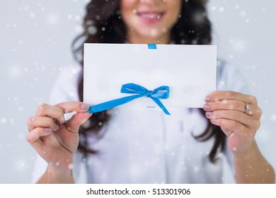 Close up of doctor holding blank white gift card over gray background and snow