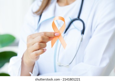 Close up of a doctor holding and showing orange awareness ribbon in her hands - Shutterstock ID 2141801221