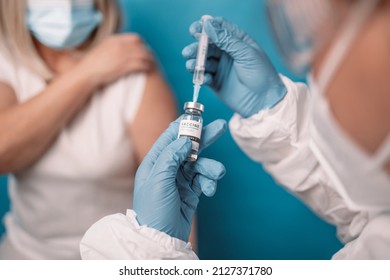 Close Up Of Doctor Or Nurse Hands Taking Covid Vaccination Booster Shot Or 3rd Dose From Syringe Over Bright Blue Color Background