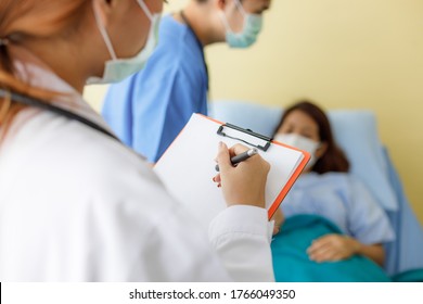 Close Up The Doctor Is Recording The Condition Of The Patient. Asian Female And Male Doctors Wearing Masks And Uniforms Are Visiting To Check The Symptoms Of Middle-aged Female Patients Lying In Bed.